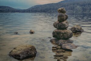 A balanced stack of stones on the edge of a calm lake with forested mountains in the background.