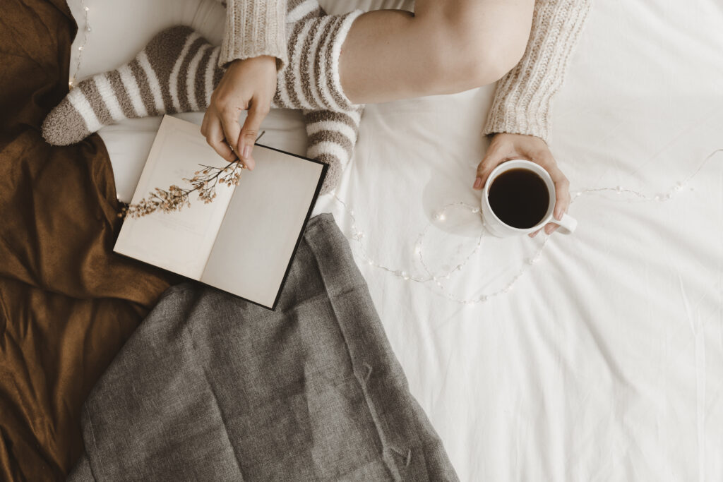 Person relaxing with a cozy sweater, striped socks, an open book, and a cup of coffee, symbolizing nervous system regulation and mindful rest.