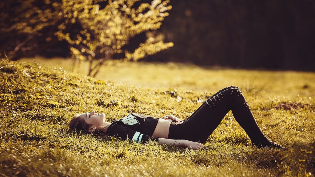 Young woman lying peacefully on a grassy field in sunlight, embodying relaxation, nervous system regulation, and connection to nature.