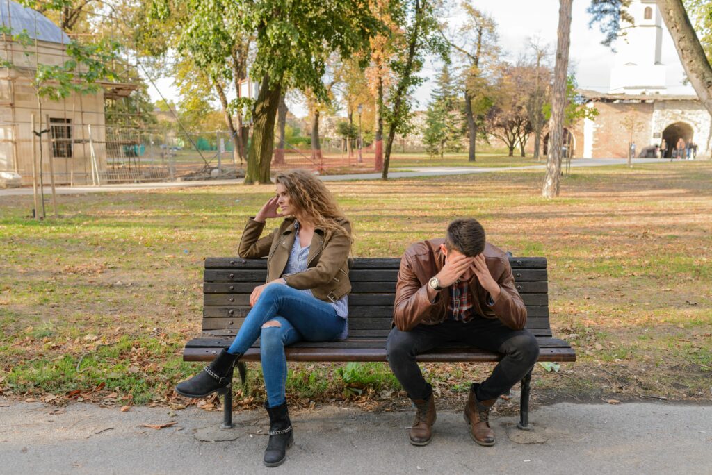 Frustrated couple sitting apart on a bench, avoiding eye contact during an argument.  
