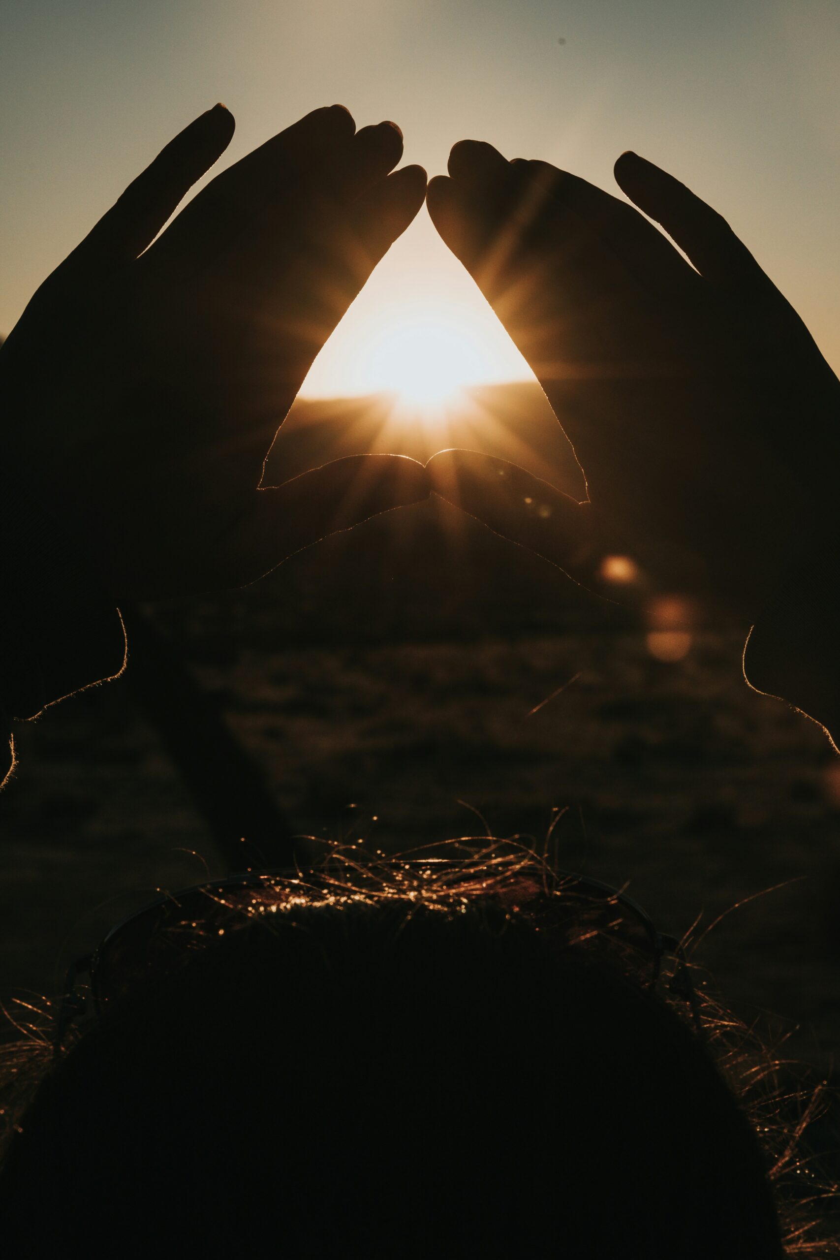 Hands framing the sun at sunset, representing deep reflection and healing in therapy intensives